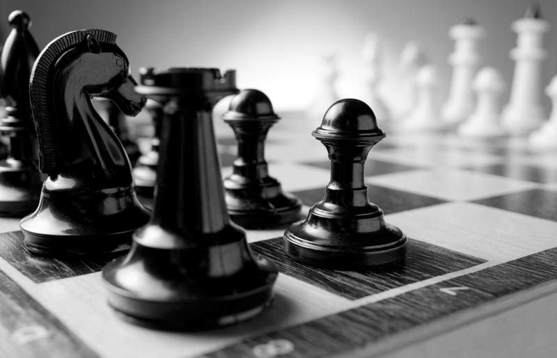 Des pièces d’échecs sont rangées sur un échiquier, les noires à l’avant-plan et les blanches à l’arrière-plan.