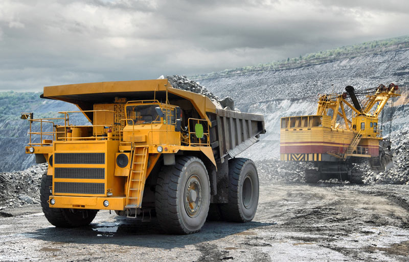 A large yellow dump truck and an excavator work in an open pit mine.