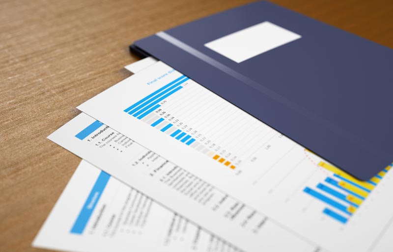 Printouts featuring reports and bar graphs are arranged on a table fanning out from a blue folder. 