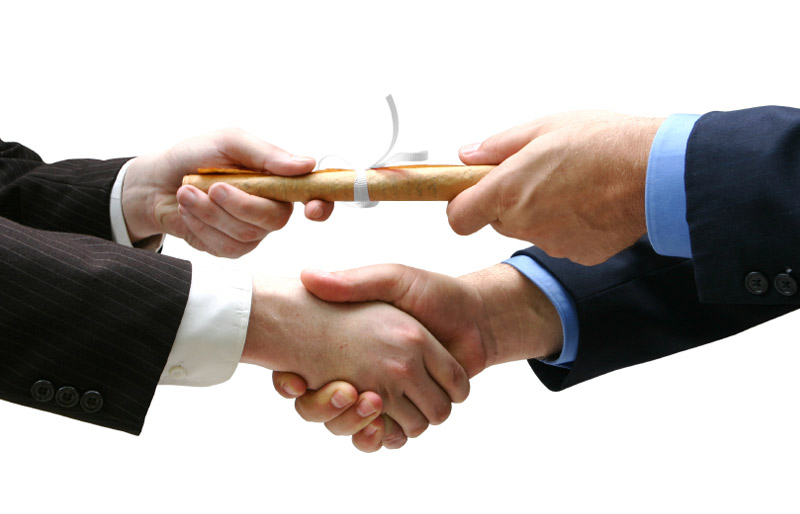 Close-up of a young man’s hand shaking an older man’s hand, above which they are each holding one end of a rolled up certificate or diploma.