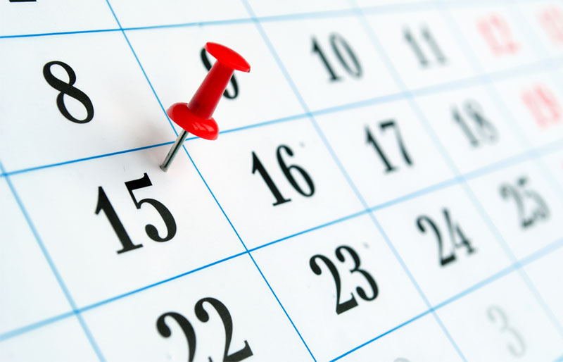 A red thumbtack is pressed into a calendar square indicating the fifteenth of the month.