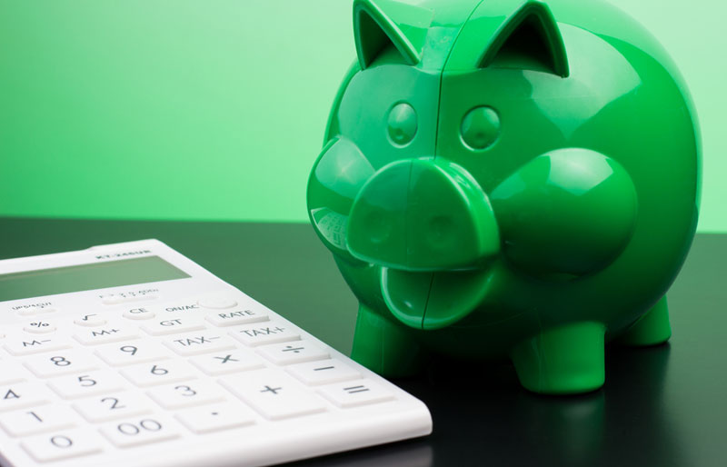 A calculator and a green piggy bank are on a table.