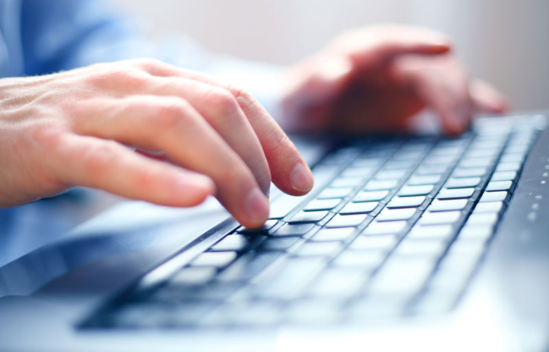 Close-up of a man’s hands typing on a computer keyboard.