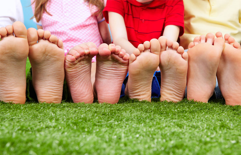 Close-up of a father, daughter, son and mother’s bare feet as they are seen sitting side-by-side in the grass.