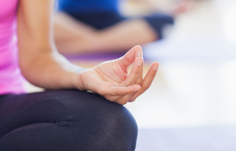 Close-up of a woman’s hand as she is in the lotus position at a yoga class.