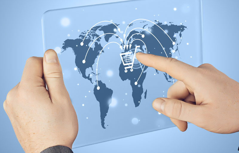 Gros plan sur les mains d'une personne qui utilise une tablette numérique futuriste, sur laquelle se trouvent des illustrations représentant le commerce électronique international.