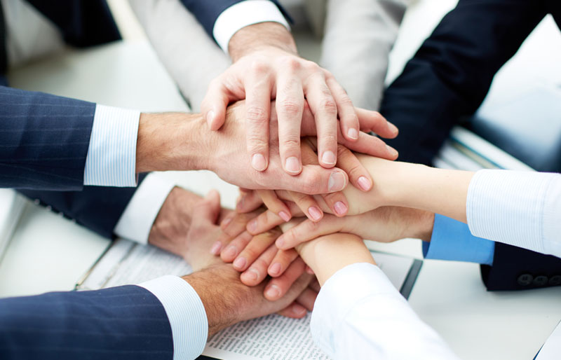 Businessmen and businesswomen perform a hand-over-hand team huddle. 