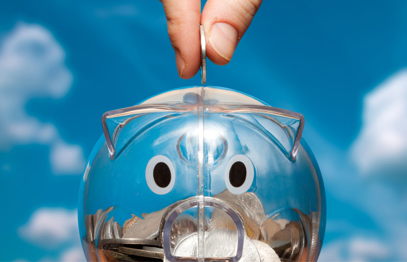 A hand drops a coin into a transparent piggy bank that appears half full.