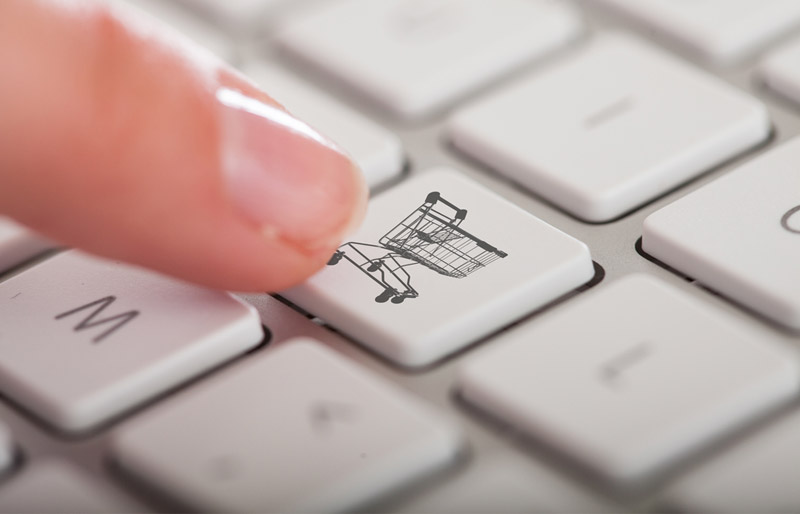 Close-up of a finger pressing a computer keyboard key featuring the image of a shopping basket.