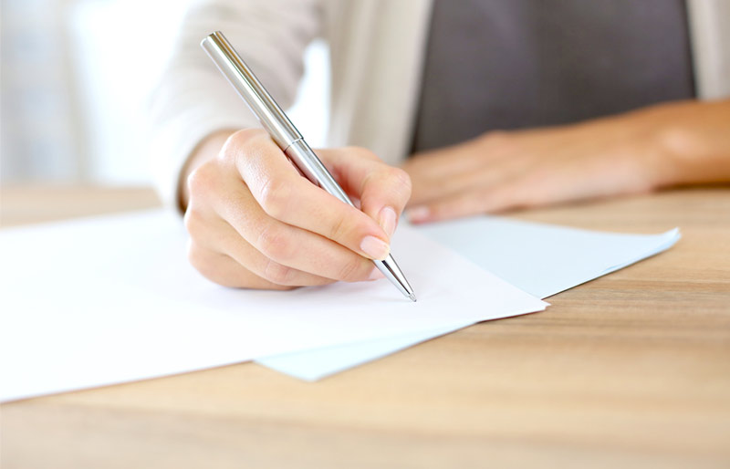 Installée à son bureau, une femme munie d’un stylo écrit sur une feuille de papier blanche.