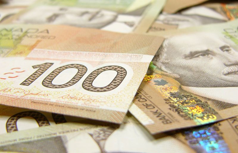 Gros plan sur des billets de 100 dollars canadiens éparpillés sur une table.