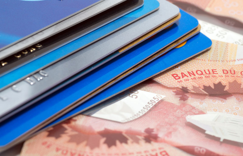 Gros plan sur une pile de cartes de crédit posée sur des billets de banque canadiens.