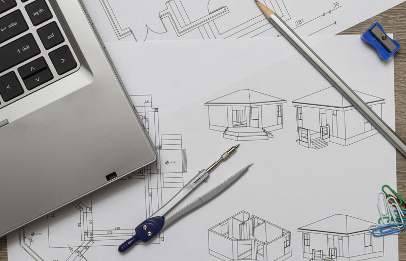 Laptop, pencil and protractor sitting on architecture drawings of a house