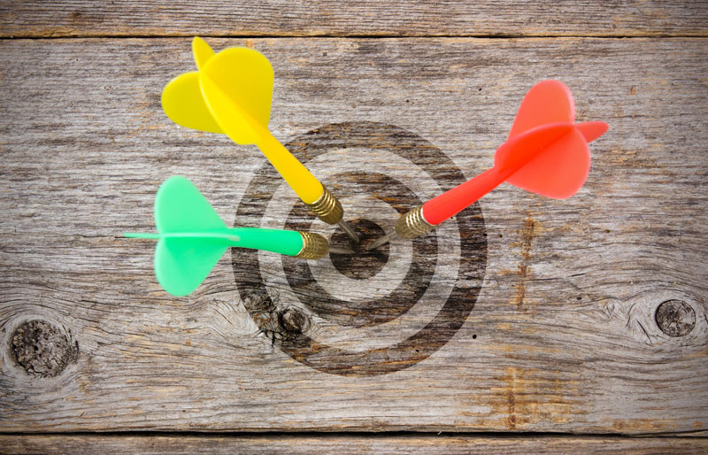 Colourful darts hitting bulls-eye of target on wooden background