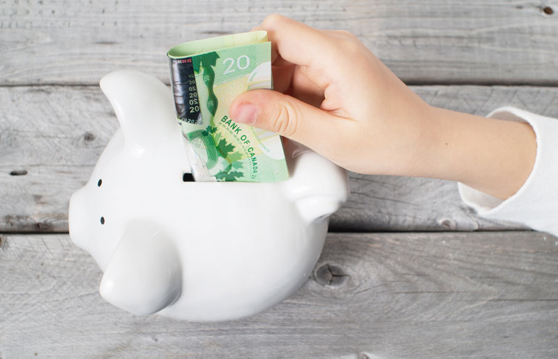 Child putting Canadian 20 dollar bills into a piggy bank