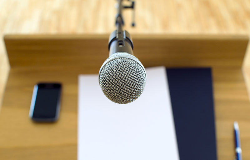 Vue plongeante sur un pupitre de conférence doté d’un microphone et sur lequel sont posées des notes.