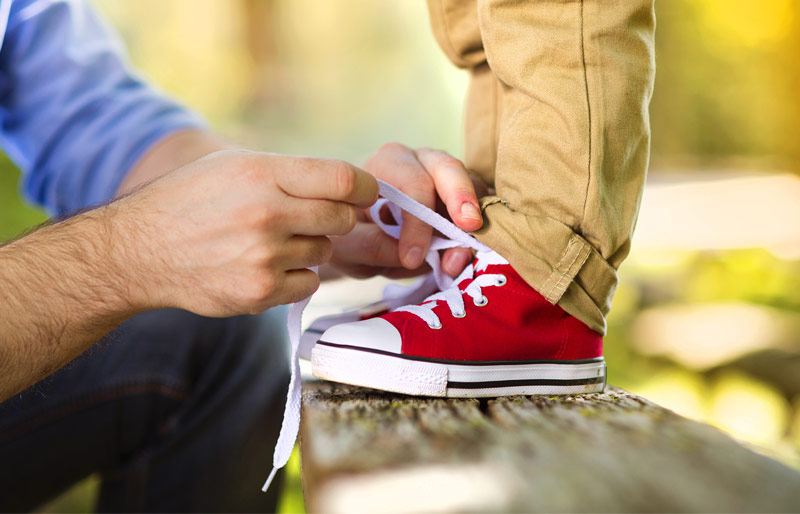Father tying shoes of child standing on park bench