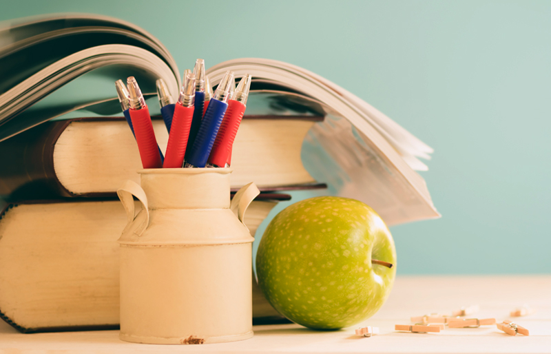 School text books, jar of pencils and an apple on a desk