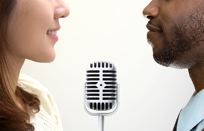 Two people facing other with a microphone between them.