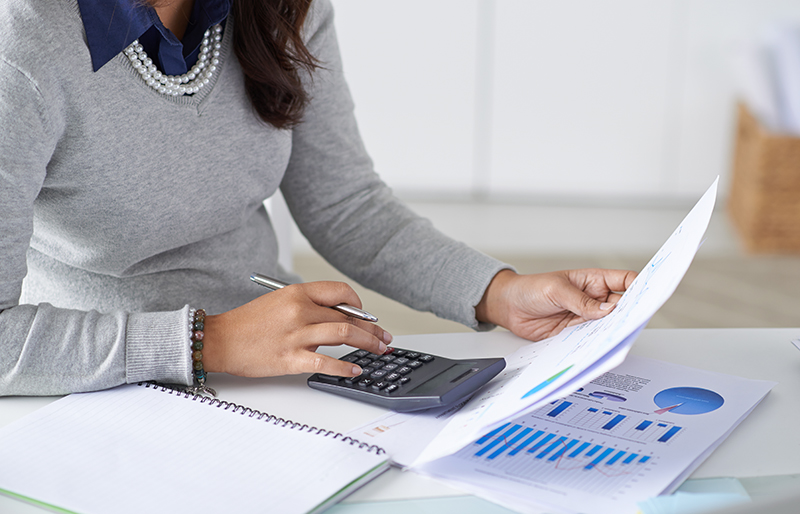Une professionnelle utilise une calculatrice pendant qu'elle consulte des documents financiers.