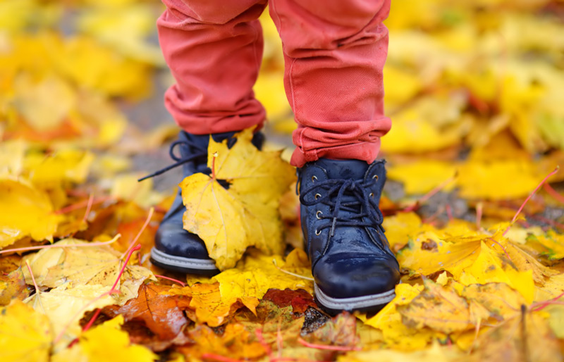 Close up of child's feet, wearing black lace-up boots and red pants, standing in pile of yellow leaves.