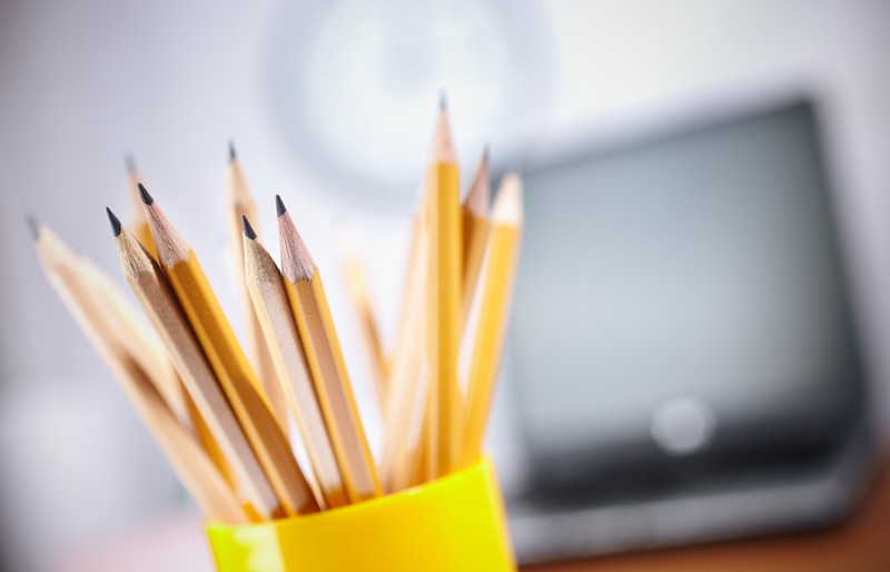 Close up of container of pencils in front of a laptop.