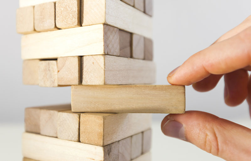 Close up of a precariously stacked pile of blocks as a person removes one block near the bottom.