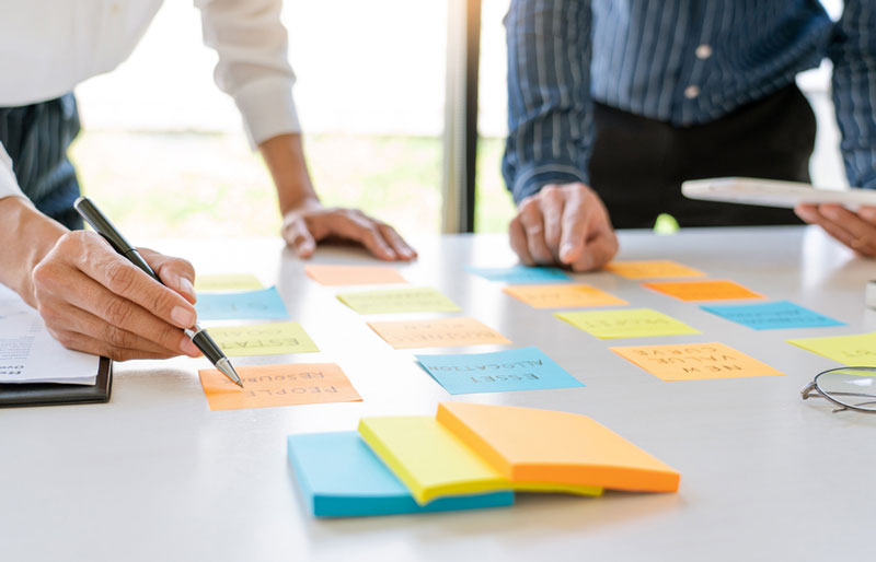 Businesspeople consult coloured sticky notes on a desk.