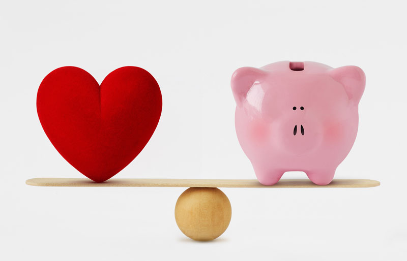 A heart and a piggy bank balancing on each side of a teeter totter.