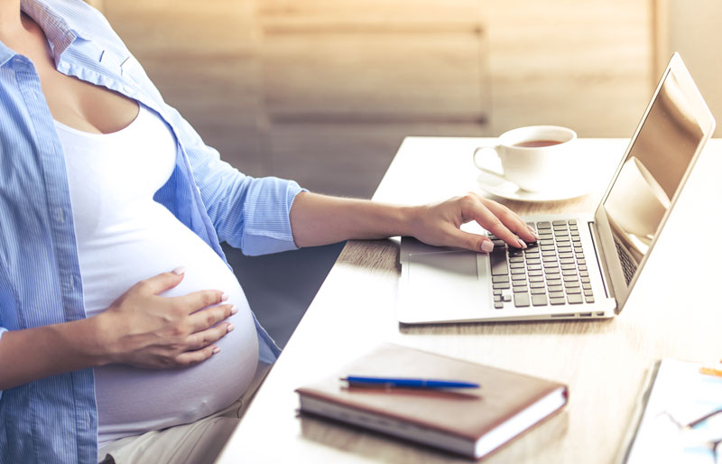 Une femme enceinte, assise à un bureau, consulter un ordinateur portable.