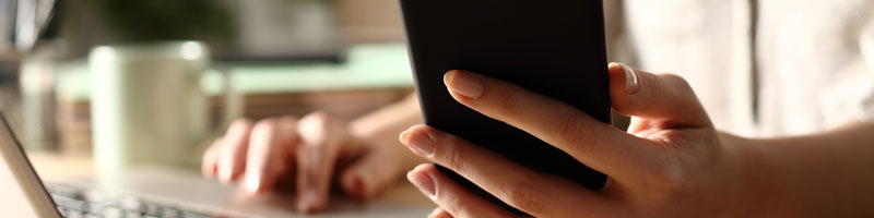 Close up of person checking a smart phone while working on a laptop.