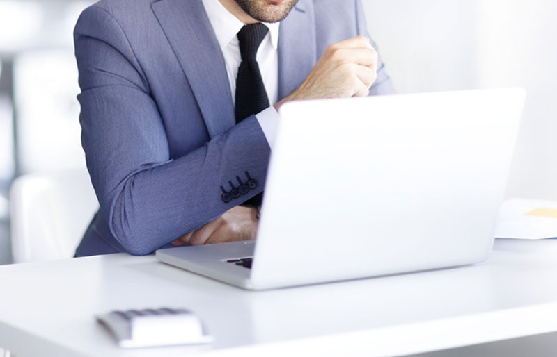 Business man in blue suit concentrating on laptop with calculator