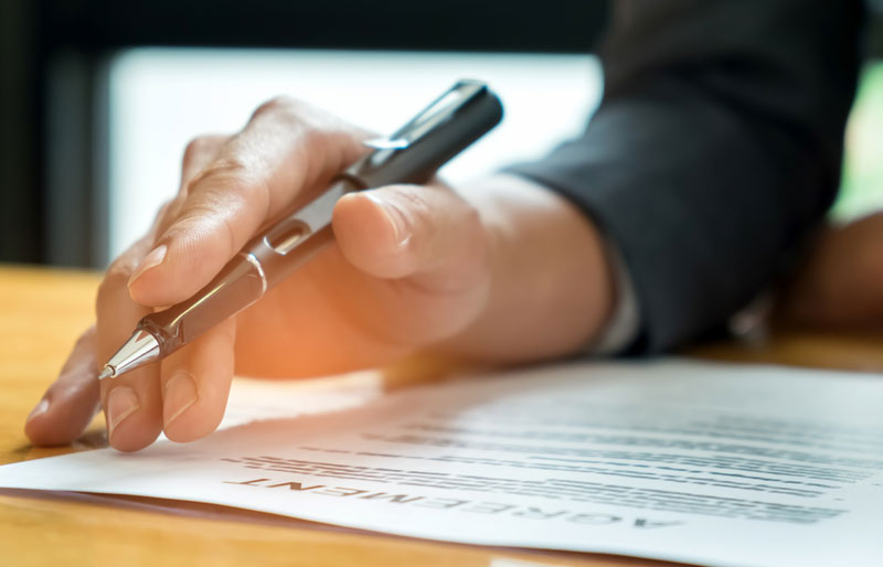 Business hand holding a pen on top of an agreement paper 