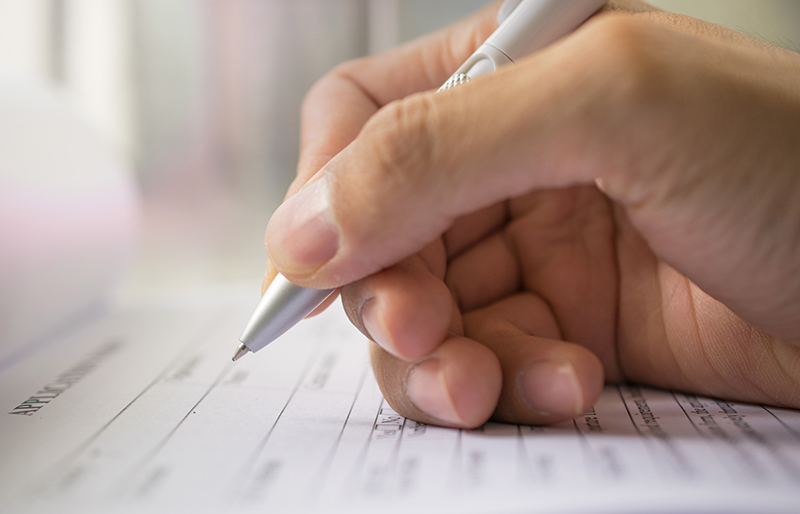 Gros plan sur la main d’un professionnel remplissant un formulaire à l’aide d’un stylo.