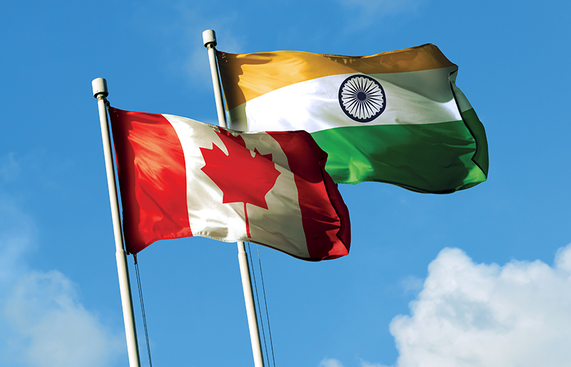 Flags for both Canada and India waving together in the breeze against a blue sky