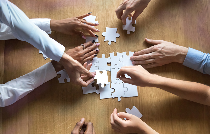 The hands and arms of a group of business people assembling a puzzle together