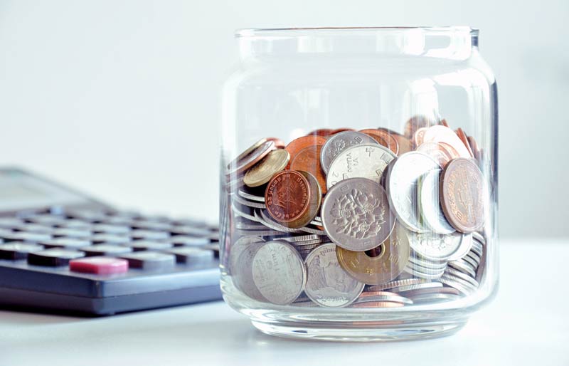 Une calculatrice à côté d’un bocal de verre rempli de pièces de monnaie de divers pays.