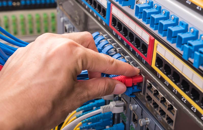 Gros plan sur les mains d’un spécialiste des TI qui branche un câble Ethernet dans un serveur de réseau.