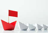 A red paper boat leading a row of smaller, white paper boats.  
