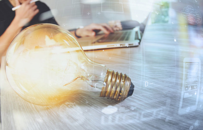L’innovation et la stratégie sont illustrées par l’image d’une ampoule électrique allumée reposant sur un bureau où une personne travaille sur son ordinateur.
