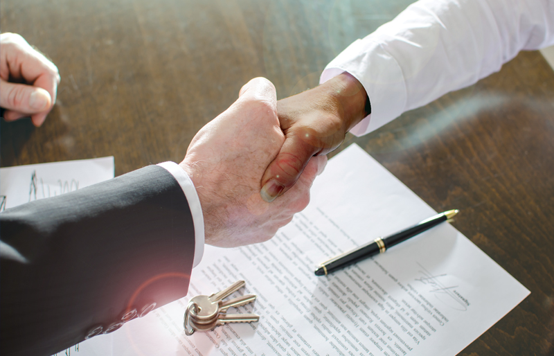 Business woman shaking the hand of another business person, over desk with a signed contract and keys