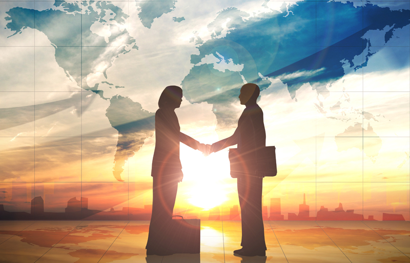 Silhouette of two business people shaking hands against a map of the world over a cityscape at sunset 