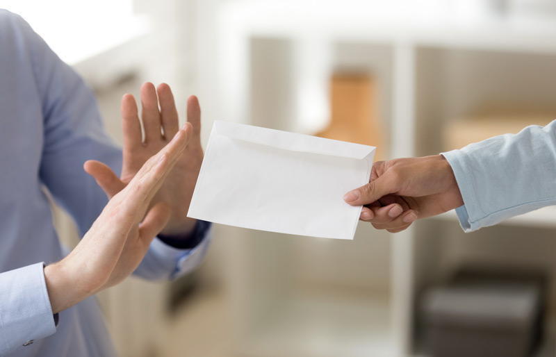 Un professionnel offre une enveloppe à un autre, qui la refuse avec les mains dans un geste de recul