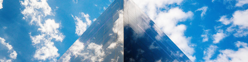 View of a building with mirrored windows reflecting the blue, partly cloudy sky.