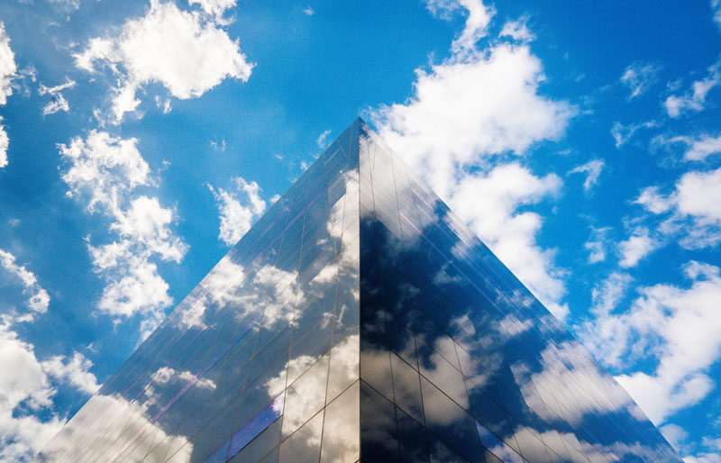 View of a building with mirrored windows reflecting the blue, partly cloudy sky.