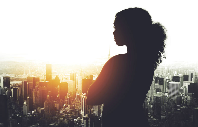 Cadrage sur la silhouette d’une professionnelle qui regarde une ville au lever du soleil.