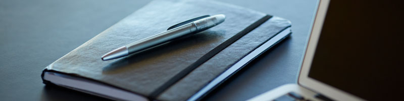 Cadrage sur un calepin de notes, un stylo et un ordinateur portable posés sur un bureau de travail