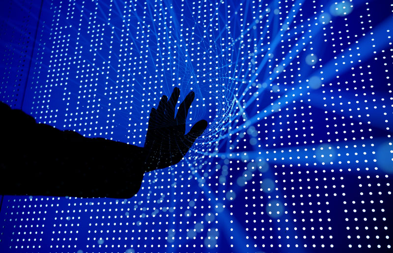 Silhouette d'une main tendue vers un écran d'ordinateur avec motif à points.