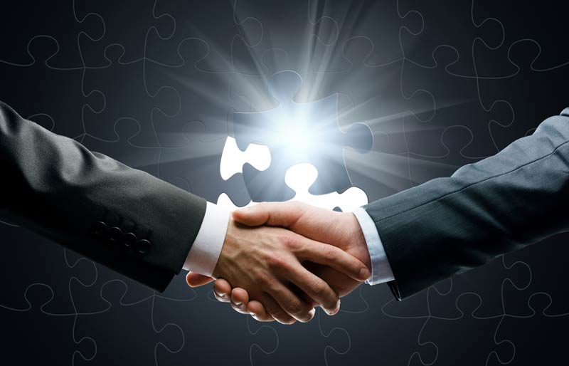 Two Accountants shaking hands over a piece of a puzzle.