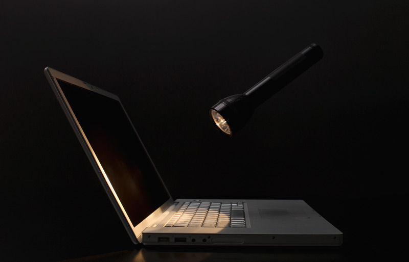 A flashlight shines on an open laptop in a dark room.